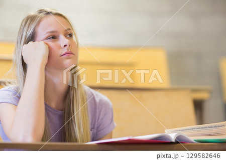 Teenage female student in purple T-shirt looking aside at open textbook on lecture desk, copy space Teenage female student in purple T-shirt looking aside at open textbook on lecture desk, copy space 129582646