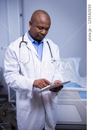 African American male physician reviewing tablet in hospital room with stethoscope and bed linens African American male physician reviewing tablet in hospital room with stethoscope and bed linens 129582650