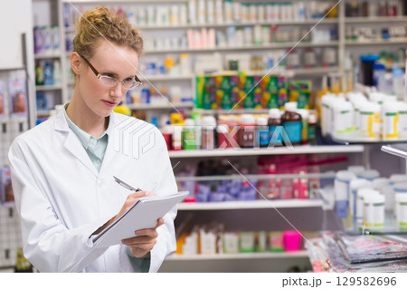 Female pharmacist writing on notepad with pen at pharmacy counter wearing lab coat, copy space Female pharmacist writing on notepad with pen at pharmacy counter wearing lab coat, copy space 129582696