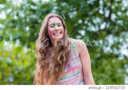 Teenage girl smiling outdoors in park festival, showing colored powder on face and arms Teenage girl smiling outdoors in park festival, showing colored powder on face and arms 129582710