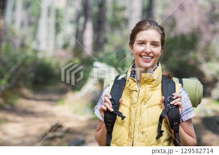 Woman standing on forest trail wearing yellow vest and holding hiking backpack with sleeping mat Woman standing on forest trail wearing yellow vest and holding hiking backpack with sleeping mat 129582714
