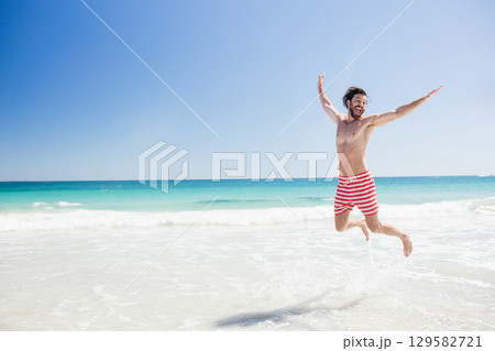 Male jumping in shallow shoreline water wearing red and white striped swim trunks, copy space Male jumping in shallow shoreline water wearing red and white striped swim trunks, copy space 129582721