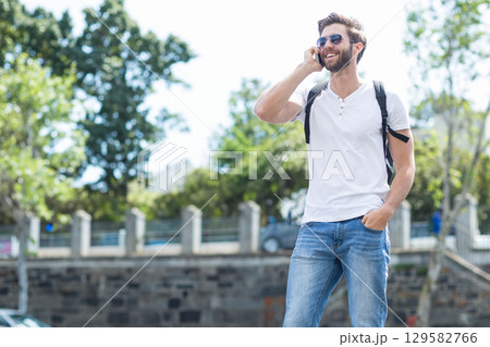 30s man talking on smartphone by stone railing with backpack, sunglasses on walkway, copy space 30s man talking on smartphone by stone railing with backpack, sunglasses on walkway, copy space 129582766