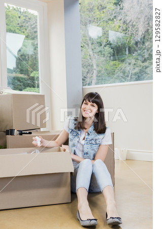 Woman sitting on living room floor packing crumpled paper into cardboard boxes with marker and mugs Woman sitting on living room floor packing crumpled paper into cardboard boxes with marker and mugs 129582827