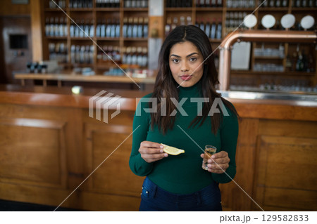Hispanic woman holding lemon wedge and shot glass at bar counter with liquor bottles, beer taps 129582833