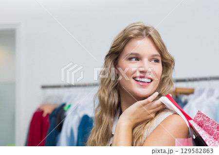 Woman smiling and holding colorful shopping bags over shoulder in retail clothing store, copy space Woman smiling and holding colorful shopping bags over shoulder in retail clothing store, copy space 129582863