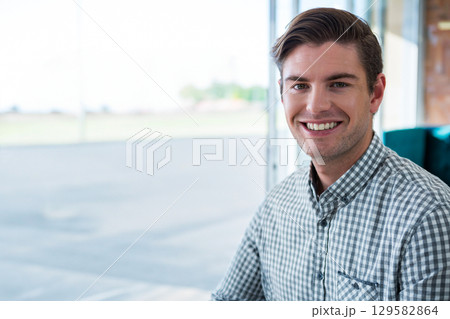 Man sitting in lounge facing camera on upholstered chair near glass windows, copy space 129582864