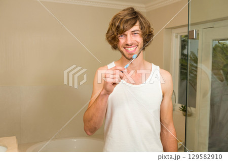 Man brushing teeth with toothbrush in bathroom near bathtub, glass shower door and potted plant Man brushing teeth with toothbrush in bathroom near bathtub, glass shower door and potted plant 129582910