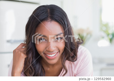 African American woman leaning forward touching face smiling at camera in kitchen with flowers 129582960