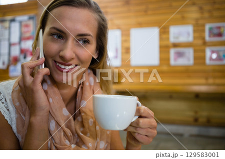 Woman in lace top sitting at cafe holding coffee cup while talking on smartphone, copy space Woman in lace top sitting at cafe holding coffee cup while talking on smartphone, copy space 129583001