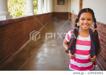 Child student standing in school corridor carrying navy backpack with hair ties, copy space 129583002