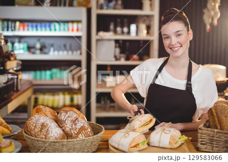 Woman bakery attendant wearing black apron arranging bread loaves in baskets on counter, copy space Woman bakery attendant wearing black apron arranging bread loaves in baskets on counter, copy space 129583066