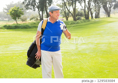 Senior man smiling while carrying golf bag, wearing golf glove, flat cap on golf course fairway Senior man smiling while carrying golf bag, wearing golf glove, flat cap on golf course fairway 129583084