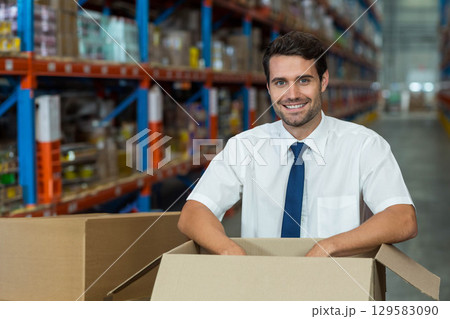 Male supervisor in business attire inspecting cardboard box in warehouse aisle among shelves Male supervisor in business attire inspecting cardboard box in warehouse aisle among shelves 129583090