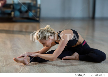 Female yogi in sportswear leaning over leg and grasping foot in fitness studio with gym equipment Female yogi in sportswear leaning over leg and grasping foot in fitness studio with gym equipment 129583095