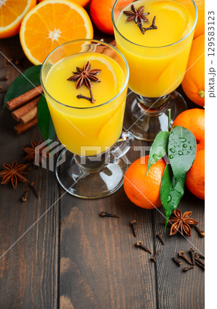 Hot spicy orange punch in glass mugs surrounded by fresh oranges, star anise, and cinnamon sticks, perfect for cozy fall winter gatherings Hot spicy orange punch in glass mugs surrounded by fresh oranges, star anise, and cinnamon sticks, perfect for cozy fall winter gatherings 129583123