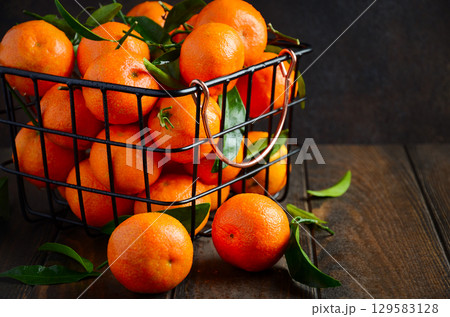 Fresh tangerines in a wire basket with green leaves, showcasing vibrant colors and natural textures, perfect for healthy lifestyle concepts Fresh tangerines in a wire basket with green leaves, showcasing vibrant colors and natural textures, perfect for healthy lifestyle concepts 129583128