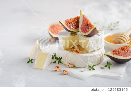 Gourmet cheese platter featuring creamy brie, fresh figs, honey, and herbs arranged beautifully on a light background for culinary delight Gourmet cheese platter featuring creamy brie, fresh figs, honey, and herbs arranged beautifully on a light background for culinary delight 129583146