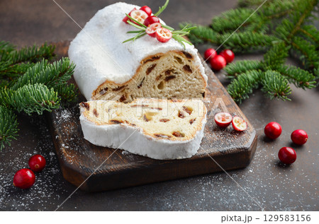 Christmas Stollen loaf with powdered sugar, sliced to reveal fruit and nut filling, surrounded by festive decorations and evergreen branches 129583156