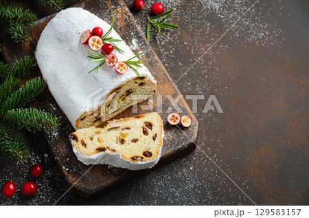 Christmas Stollen bread with powdered sugar, sliced to reveal rich texture and fruit filling, garnished with festive berries and greenery for holiday cheer Christmas Stollen bread with powdered sugar, sliced to reveal rich texture and fruit filling, garnished with festive berries and greenery for holiday cheer 129583157