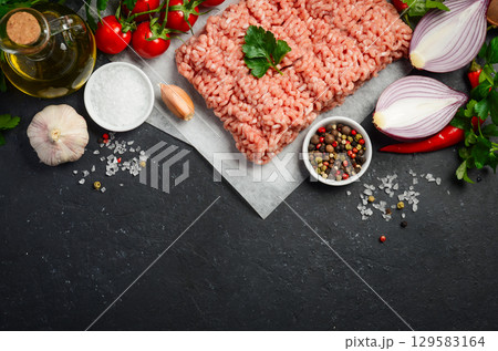Fresh pork minced meat surrounded by vibrant vegetables, spices, and herbs on a dark stone surface, perfect for culinary creations and recipes 129583164