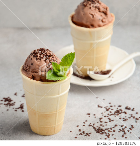 Delicious chocolate ice cream scoops in waffle cones garnished with mint leaves, served on a plate with chocolate sprinkles and a spoon Delicious chocolate ice cream scoops in waffle cones garnished with mint leaves, served on a plate with chocolate sprinkles and a spoon 129583176