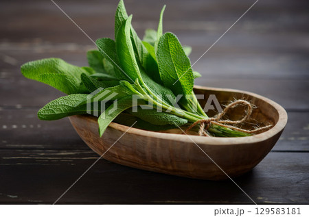 Fresh green sage leaves arranged in a wooden bowl on a rustic table, showcasing natural textures and vibrant colors for culinary use Fresh green sage leaves arranged in a wooden bowl on a rustic table, showcasing natural textures and vibrant colors for culinary use 129583181