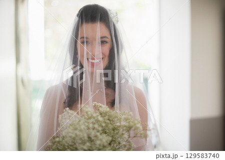 Female bride standing in bright entrance with veil, strapless gown holding bouquet of baby's breath Female bride standing in bright entrance with veil, strapless gown holding bouquet of baby's breath 129583740