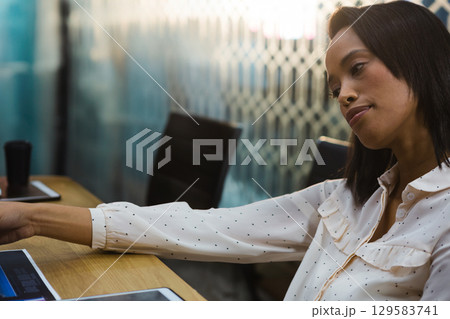 African American woman leaning and reaching across table toward tablet in meeting room, copy space 129583741