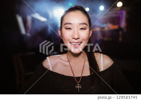 Chinese woman standing in dim event space with lights wearing black top with beaded cross necklace 129583745