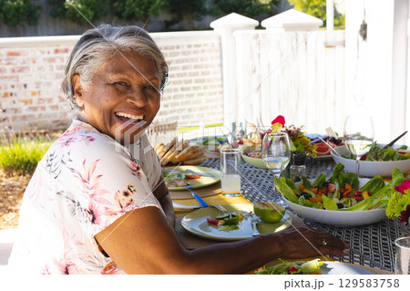 Senior African American woman smiling, sitting at patio table with salads, lemonade, copy space 129583758