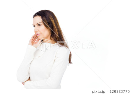 Woman standing in studio against white backdrop wearing white sweater touching jawline, copy space 129583770