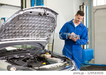Male mechanic logging engine bay data with clipboard and pen near hydraulic lift posts, copy space Male mechanic logging engine bay data with clipboard and pen near hydraulic lift posts, copy space 129583830