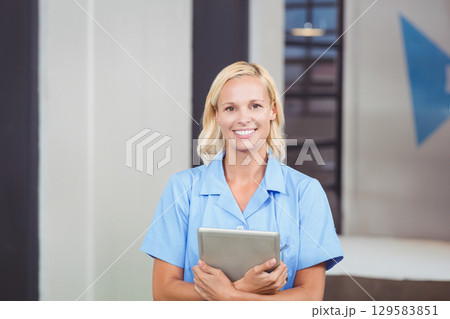 Female healthcare professional holding tablet and smiling in medical corridor near triangular sign Female healthcare professional holding tablet and smiling in medical corridor near triangular sign 129583851