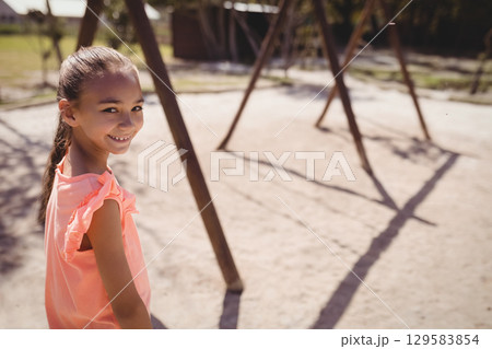 School-age girl standing on sandy playground at suburban park with wooden swing frames, copy space School-age girl standing on sandy playground at suburban park with wooden swing frames, copy space 129583854