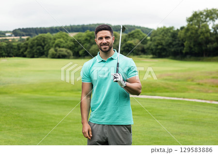 Man in his twenties holding golf club on golf fairway wearing polo shirt with golf glove 129583886