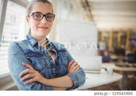 Female professional standing with arms crossed in office near whiteboard and laptop, copy space Female professional standing with arms crossed in office near whiteboard and laptop, copy space 129583900