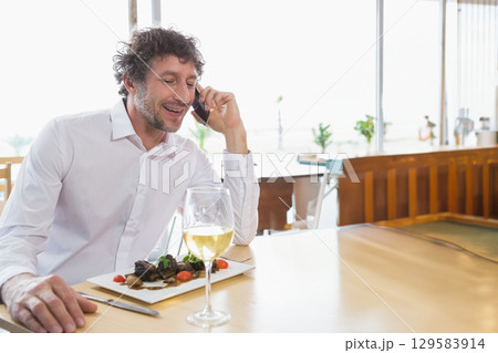 Man wearing shirt talking on smartphone at dining table with meat plate, wine glass, copy space Man wearing shirt talking on smartphone at dining table with meat plate, wine glass, copy space 129583914