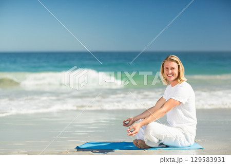 Man meditating on blue yoga mat on wet sand at beach under clear sky, copy space 129583931