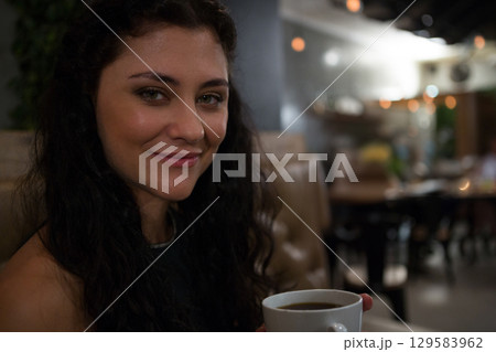 Female customer cradling white mug in tan leather booth at coffee shop, tables, plants, copy space 129583962