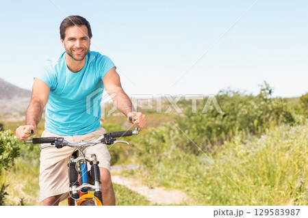 Mid adult male cyclist riding mountain bike with suspension forks along dirt trail in countryside Mid adult male cyclist riding mountain bike with suspension forks along dirt trail in countryside 129583987