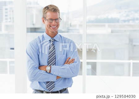 Adult male standing arms crossed before office windows wearing eyeglasses striped tie wristwatch 129584030