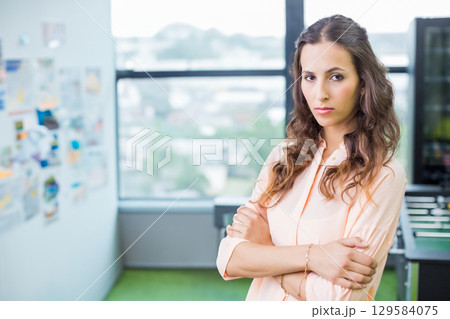 Woman in late twenties crossing arms in office showing pinboard, foosball table, copy space Woman in late twenties crossing arms in office showing pinboard, foosball table, copy space 129584075