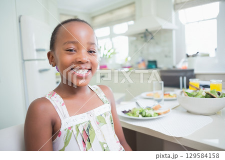 African American child girl sitting at kitchen table eating salad and drinking juice, copy space African American child girl sitting at kitchen table eating salad and drinking juice, copy space 129584158