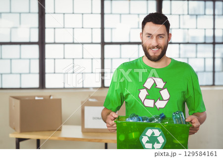 Man standing holding green recycling bin with bottles in community center sorting area, copy space 129584161