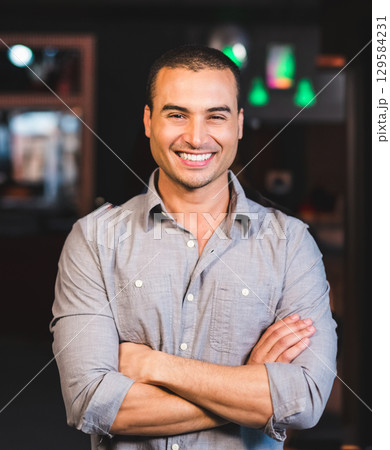 Man standing with arms crossed in softly lit lounge space with green pendant lights and shelves Man standing with arms crossed in softly lit lounge space with green pendant lights and shelves 129584231