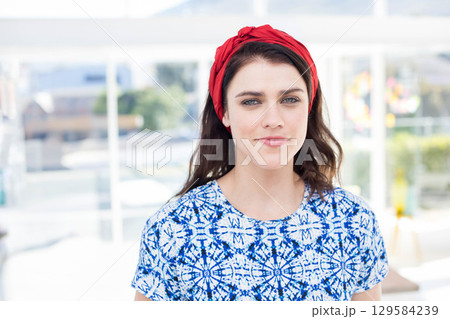 Woman in twenties standing on sunlit terrace wearing red headband and blue blouse by white railing Woman in twenties standing on sunlit terrace wearing red headband and blue blouse by white railing 129584239