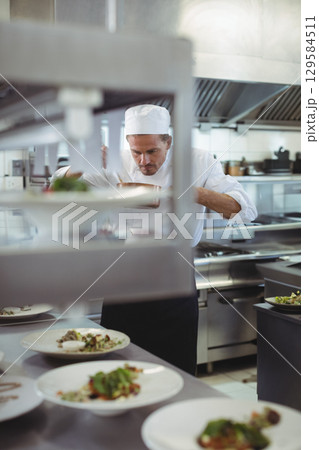 Male chef leaning over counter arranging garnishes on porcelain plates on pass rack in kitchen Male chef leaning over counter arranging garnishes on porcelain plates on pass rack in kitchen 129584511