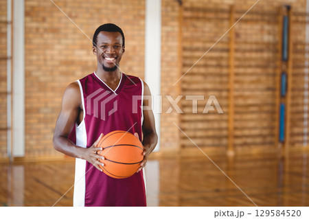 African American male holding basketball on basketball court wearing uniform near wooden wall bars 129584520