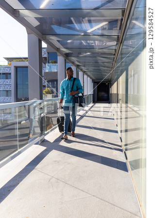 African American male checking wristwatch walking glass walkway pulling suitcase and navy duffel African American male checking wristwatch walking glass walkway pulling suitcase and navy duffel 129584527